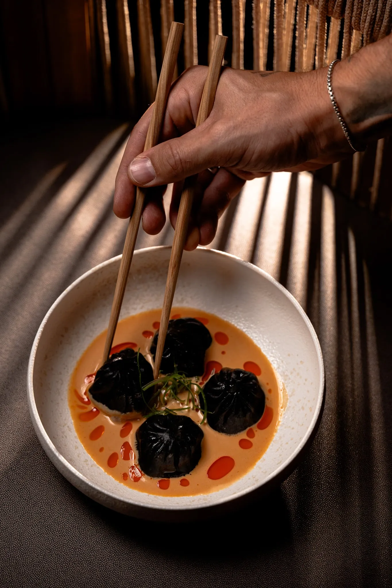 Dumplings lifted with chopsticks, with bamboo shadows across the table
