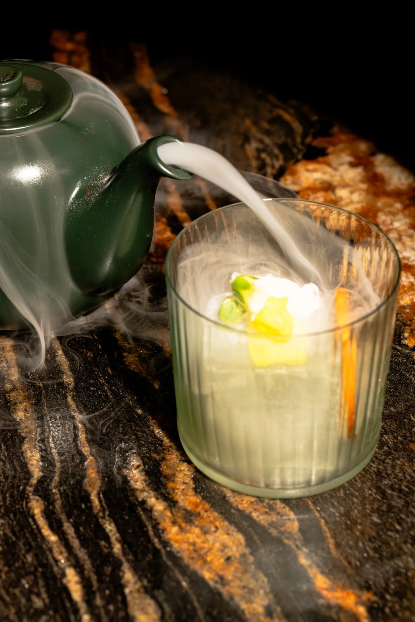 Tea poured over a cocktail, smoke spilling across the table
