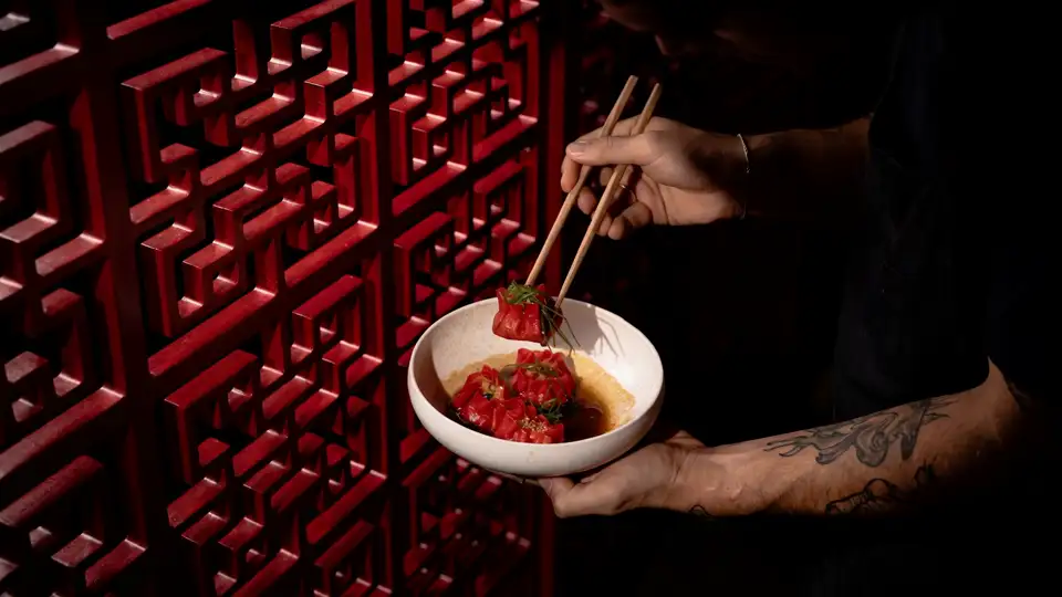 Red dumplings lifted with chopsticks against the lacquered lattice