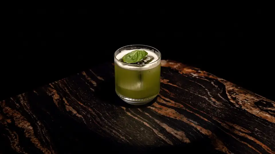 A green basil cocktail on a dark marble bar